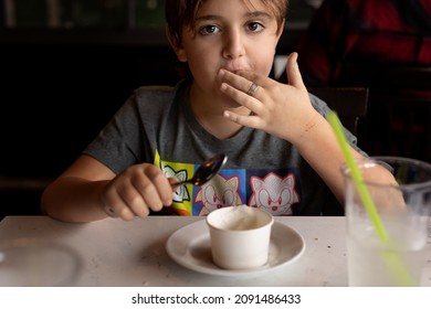 Brooklyn, NY, US - December 11, 2021 - Cute Kid Licking Fingers While Eating Dessert - Young Boy Eats Italian Ices With Spoon In Restaurant