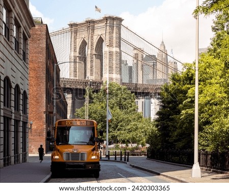 Brooklyn, USA - June 14 2023: A yellow school bus is parked in Dumbo on a sunny day with the Brooklyn bridge in the background and skyscrapers from Manhattan. No people or logos