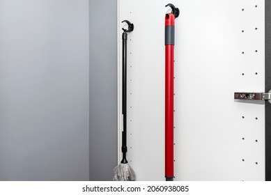 Broom and duster hanging in a built-in kitchen cupboard, black pantry door open.