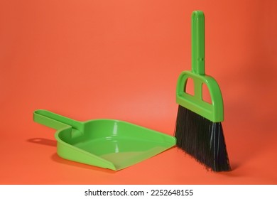 Broom and dustpan are a pair of cleaning tools. Small green broom and dustpan on orange background isolated. - Powered by Shutterstock