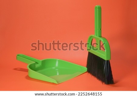 Broom and dustpan are a pair of cleaning tools. Small green broom and dustpan on orange background isolated.
