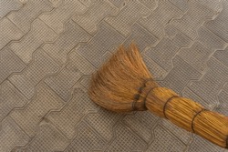 A Broom Made Of Natural Dry Branches, Tall And Durable Plants, Sweeps The Relief Surface Of The Pavement, Laid Out Of Paving Stones In The Shape Of A Bowtie-like Tie.