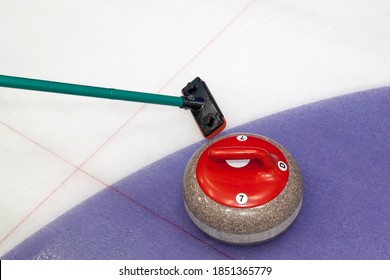 Broom and stone for curling. view of red curling stone in outer blue ring of house with broom nearby