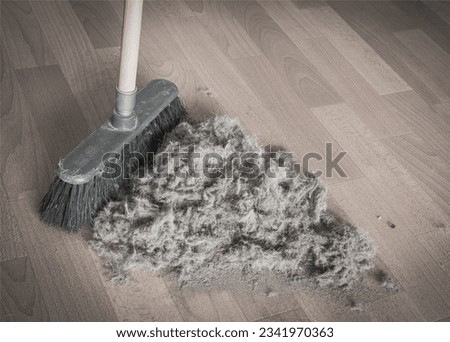 broom sweeping up a giant mixed pile of dust, sand and wool