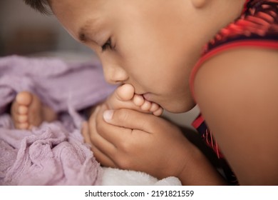 Brother Holding And Kissing Newborn Sister Foot, Lifrestyle Portrait At Natural Light, Babyhood And Childhood Concept - Image