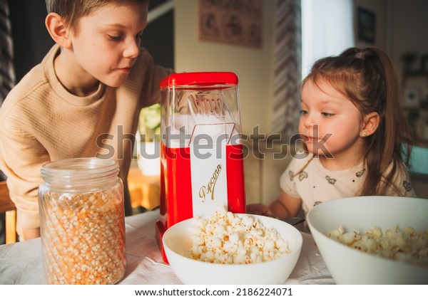 brother and sister cook popcorn at home in a\
popcorn maker. Girl is waiting for popcorn to start flying out of\
the popcorn machine