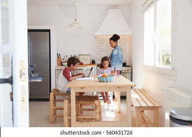 Brother And Sister Doing Homework In Kitchen While Mum Cooks