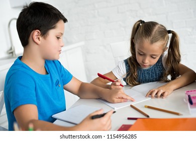 brother and sister doing homework together at table at home - Shutterstock ID 1154956285