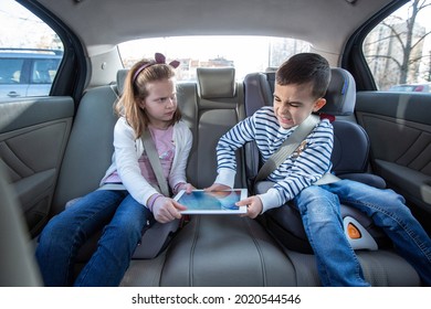 Brother and sister fighting over digital tablet on the back seat of the car, kids concept - Shutterstock ID 2020544546
