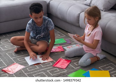 Brother And Sister Getting Ready For Back To School. Focused Boy And Girl In Casual Clothes Putting Covers On New Copybooks While Sitting On Floor In Living Room