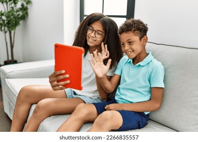 Brother and sister having video call using touchpad sitting on sofa at home