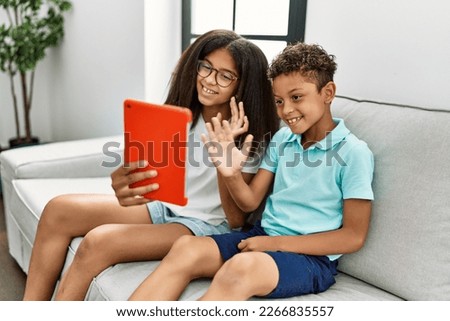 Brother and sister having video call using touchpad sitting on sofa at home