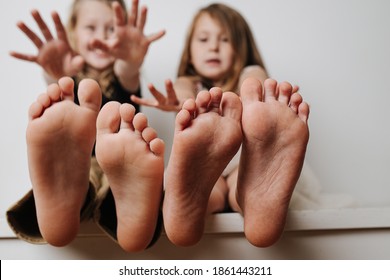 Brother And Sister Holding Bare Feet Close Up To The Camera. Their Blurred Faces In A Background. Hands Reaching To Camera.