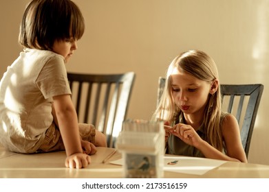 Brother and sister at home at the table and draw. The older sister teaches her brother to draw, the little boy watches the older sister draw. A friendly creative family - Shutterstock ID 2173516159
