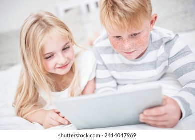 Brother and sister lying in bed using tablet - Powered by Shutterstock