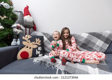 Brother And Sister In Matching White-red Pajamas Pose On The Couch In Their Playroom.