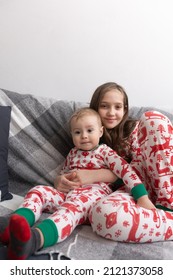 Brother And Sister In Matching White-red Pajamas Pose On The Couch In Their Playroom.