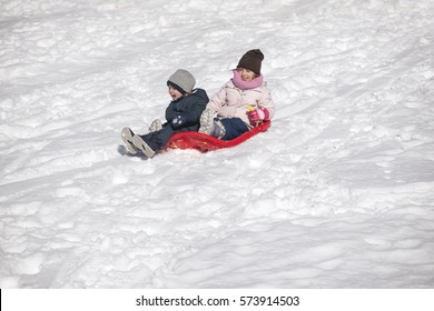 Brother And Sister On Toboggan On Snow Covered Hill