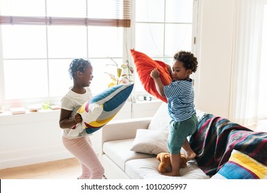 Brother and sister pillow fighting in living room