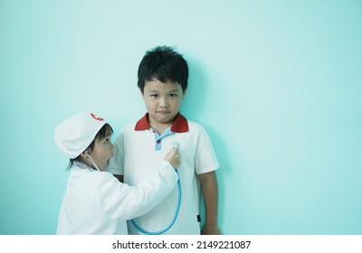 Brother and sister are playing doctor and hospital using stethoscope toy and medical uniform at home. Soft focus.