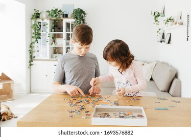 Brother and sister playing puzzles at home. Children connecting jigsaw puzzle pieces in a living room table. Kids assembling a jigsaw puzzle. Fun family leisure. Stay at home activity for kids.