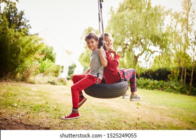 Brother And Sister Playing In Tire Swing In Garden At Home