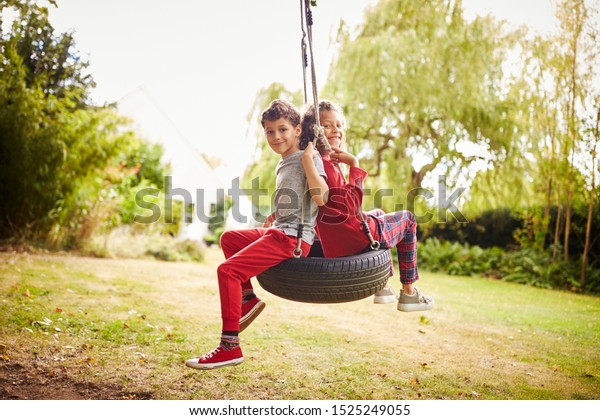 Brother And Sister Playing In Tire Swing In Garden\
At Home