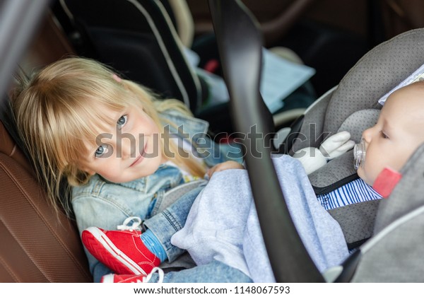 Brother and sister sitting in car\
in safety seat. Siblings on passenger places having fun together\
during travel by vehicle. Travelling with children\
concept