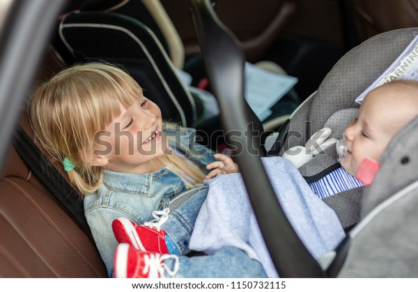 Brother and sister sitting in car\
in safety seat. Siblings on passenger places having fun together\
during travel by vehicle. Travelling with children\
concept