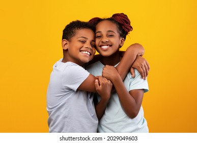 Brotherhood, sisterhood, siblings, twins relationaships, family concept. Loving cheerful black boy brother hugging his pretty smiling older sister, cuddling over yellow studio background