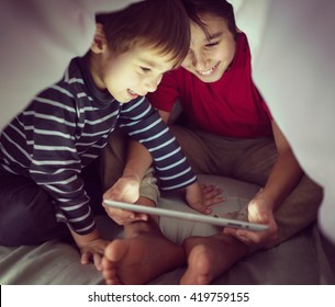 Brothers Kids With Tablet Computer Under Blanket At Night In A Dark Room