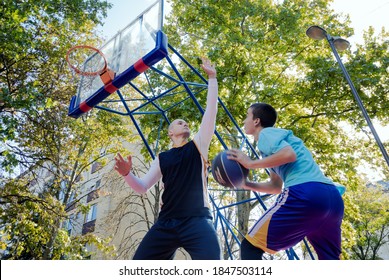 Brothers playing basketball One On One on outdoor court. Shooting at the hoop and jumping to block shot. Side view under the basketball hoop. Sport and healthy lifestyle.