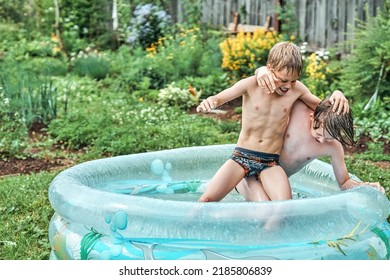 Brothers wrestle in children inflatable pool in cottage yard against lush greenery and flowers. Cheerful schoolboys have fun in water on summer in countryside. No logo - Shutterstock ID 2185806839