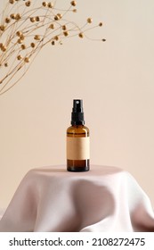 Brown amber glass spray bottle with label mockup and dry flowers on dais podium on  beige background.