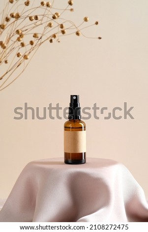 Brown amber glass spray bottle with label mockup and dry flowers on dais podium on  beige background.