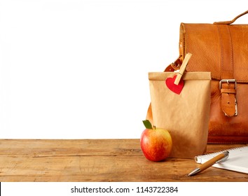 Brown Bag Lunch, Fruit, Notebook, Pen And Leather Purse Or Backpack On Table. Includes Copy Space Over White.