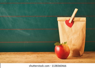 Brown Bag Lunch And Red Apple Over Green Background With Table For Nutrition Theme