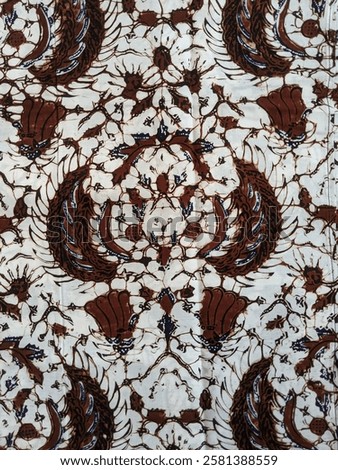 Brown batik cloth with a main pattern resembling a flower or crown with carved accents on the side. A white background with dark brown branching patterns adds depth to the design. 