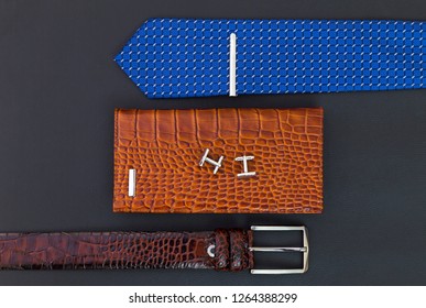 Brown Belt, Wallet, Blue Tie With Metal Pin And Cuff Links On Black Leather Surface. Fashion Concept