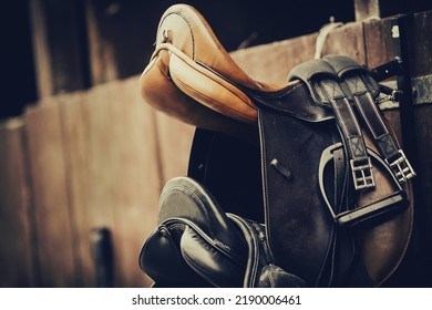 Brown and black saddles hang on the stall. Horse ammunition. Equestrian sport.