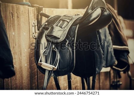 Brown and black saddles hang on the stall. Horse ammunition. Equestrian sport.
