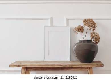 Brown bold vase. Dry hydrangea flowers on old wooden bench. Blank black picture frame mockup. White wall moulding background, stucco decor. Empty copy space. Elegant interior. Summer, fall still life  - Shutterstock ID 2142198821