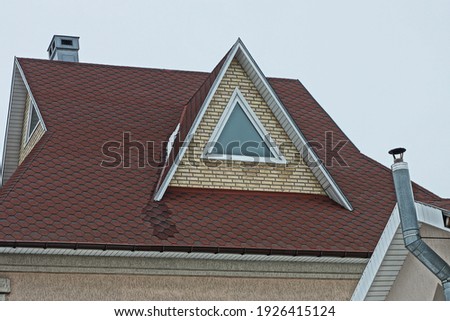brown brick attic with one triangular window on the tiled roof of a private house against a gray sky