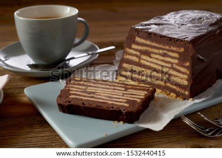 Brown butter biscuit cake with chocolate icing, served with coffee on blue ceramic tray. Close-up view on wooden table