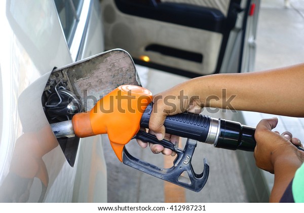 Brown car\
with Orange Fuel nozzle on a gas\
station\
