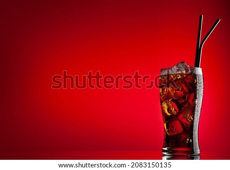 A brown carbonated drink. Fresh cold sweet cola beverage with ice cubes. Over red background with copy space