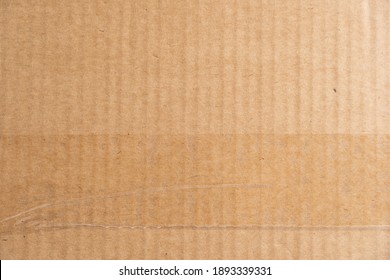 Brown cardboard texture with a transparent adhesive tape strip and some wrinkles. Carton structure of a packaging box used for shipping and delivery.