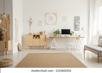 Brown carpet between pouf and grey sofa in white home office interior with chair at desk. Real photo - Shutterstock ID 1151842352