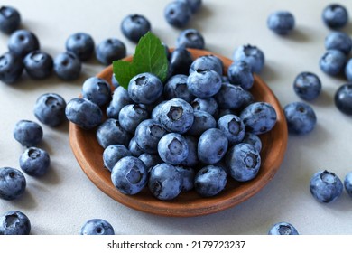 Brown ceramic bowl of fresh ripe blueberries with green leaves on kitchen table - Powered by Shutterstock