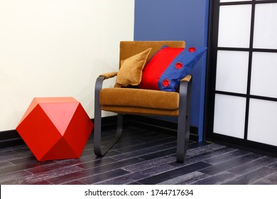 A Brown Chair With Two Pillows. Bright Tones Of The Children's Room, Red, White, Blue, Brown. Children's Toy, Built-in Duffcase Cabinet.